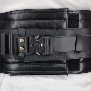 May include: Black leather belt with a heavy-duty buckle and a series of small loops. The belt features a hook-and-loop closure and is designed for durability. The buckle has a gold-colored accent.