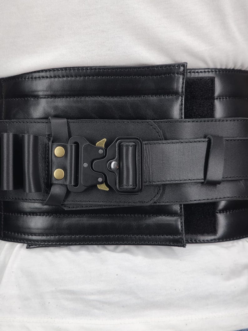 May include: Black leather belt with a heavy-duty buckle and a series of small loops. The belt features a hook-and-loop closure and is designed for durability. The buckle has a gold-colored accent.