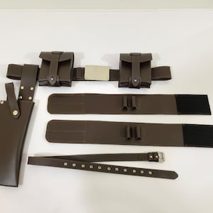 K&ouml;nnte beinhalten: Ein braunes Leder-Utility-G&uuml;rtel-Set mit Taschen, einer Messerscheide und zus&auml;tzlichen G&uuml;rtelkomponenten. Das Set enth&auml;lt einen Hauptg&uuml;rtel mit zwei Taschen, zwei zus&auml;tzliche G&uuml;rtel mit Schlaufen und einen separaten G&uuml;rtel mit einer Schnalle.