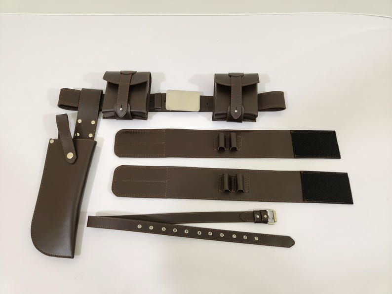 K&ouml;nnte beinhalten: Ein braunes Leder-Utility-G&uuml;rtel-Set mit Taschen, einer Messerscheide und zus&auml;tzlichen G&uuml;rtelkomponenten. Das Set enth&auml;lt einen Hauptg&uuml;rtel mit zwei Taschen, zwei zus&auml;tzliche G&uuml;rtel mit Schlaufen und einen separaten G&uuml;rtel mit einer Schnalle.