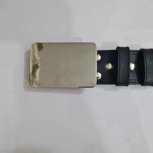 K&ouml;nnte beinhalten: Schwarzer Lederg&uuml;rtel mit einer rechteckigen, silberfarbenen Schnalle. Der G&uuml;rtel hat zwei Schlaufen und ist mit silbernen Nieten befestigt. Die N&auml;hte sind an den Kanten sichtbar und verleihen dem Design Details. Der G&uuml;rtel ist ca. 3,8 cm breit.