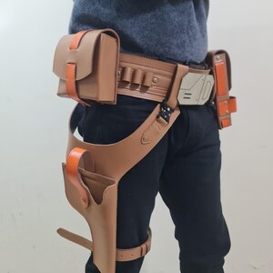 May include: A brown leather utility belt with orange detailing, including multiple pouches and a holster. The belt has a leg strap and a decorative buckle. The design is reminiscent of a sci-fi or cosplay accessory.