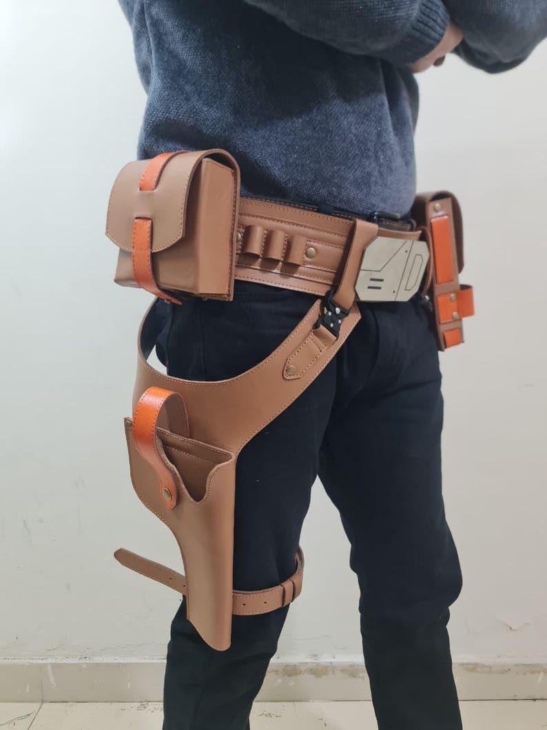 May include: A brown leather utility belt with orange detailing, including multiple pouches and a holster. The belt has a leg strap and a decorative buckle. The design is reminiscent of a sci-fi or cosplay accessory.