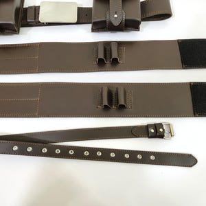 K&ouml;nnte beinhalten: Brauner Leder-Utility-G&uuml;rtel mit Taschen, einer silbernen Schnalle und einem separaten G&uuml;rtel mit &Ouml;sen. Der G&uuml;rtel hat einen Klettverschluss und ist zum Tragen von Gegenst&auml;nden konzipiert. Das Leder ist mit einem Kontrastfaden gen&auml;ht.