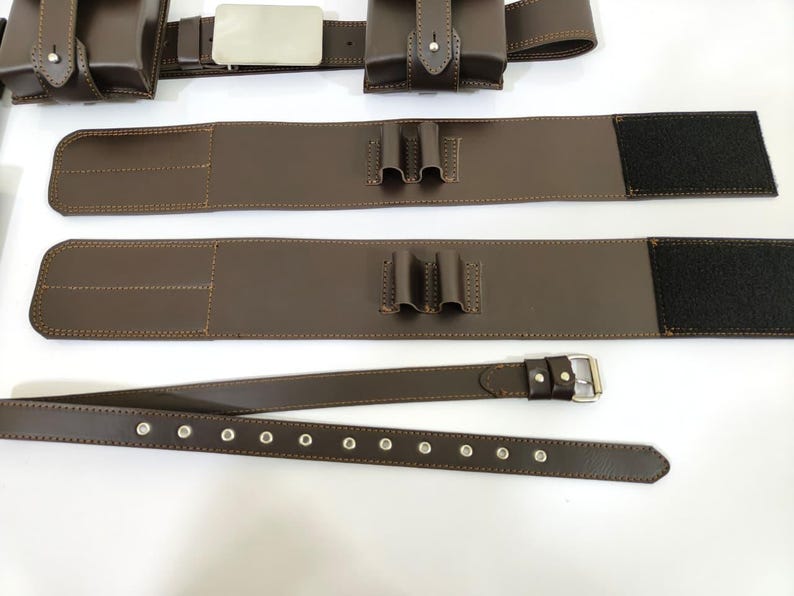 K&ouml;nnte beinhalten: Brauner Leder-Utility-G&uuml;rtel mit Taschen, einer silbernen Schnalle und einem separaten G&uuml;rtel mit &Ouml;sen. Der G&uuml;rtel hat einen Klettverschluss und ist zum Tragen von Gegenst&auml;nden konzipiert. Das Leder ist mit einem Kontrastfaden gen&auml;ht.