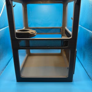 May include: A black terrarium with clear glass panels and a mesh ventilation area. A decorative rock is inside. The terrarium is designed for small reptiles or amphibians. The background is a light blue.