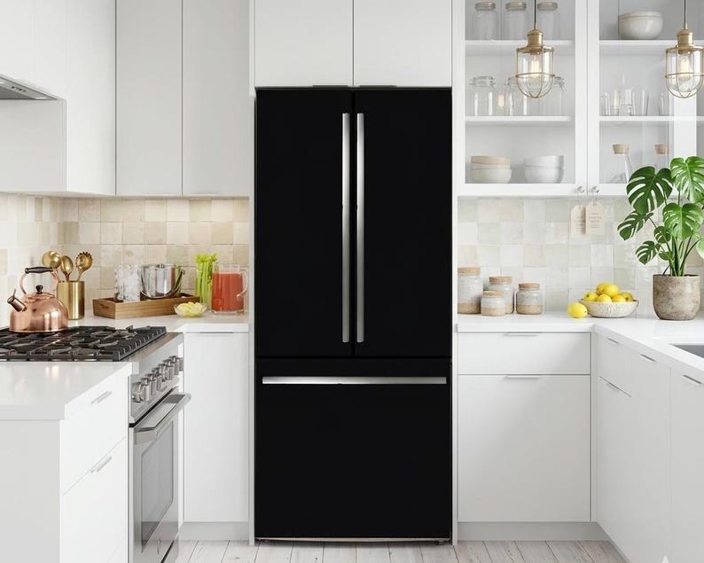K&ouml;nnte beinhalten: Ein mattschwarzer French-Door-K&uuml;hlschrank mit vertikalen silbernen Griffen an den oberen T&uuml;ren und einem horizontalen silbernen Griff an der unteren Gefrierschublade, platziert zwischen wei&szlig;en K&uuml;chenschr&auml;nken und einer wei&szlig;en Arbeitsplatte.