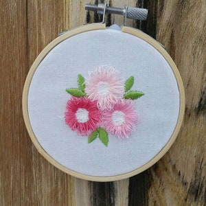 May include: A white embroidery hoop with a floral design. The flowers are pink and white with green leaves.
