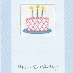 May include: A light blue card with a white border and a pink and blue embroidered cake with three yellow candles. The text "Have a Sweet Birthday!" is written in cursive at the bottom of the card.
