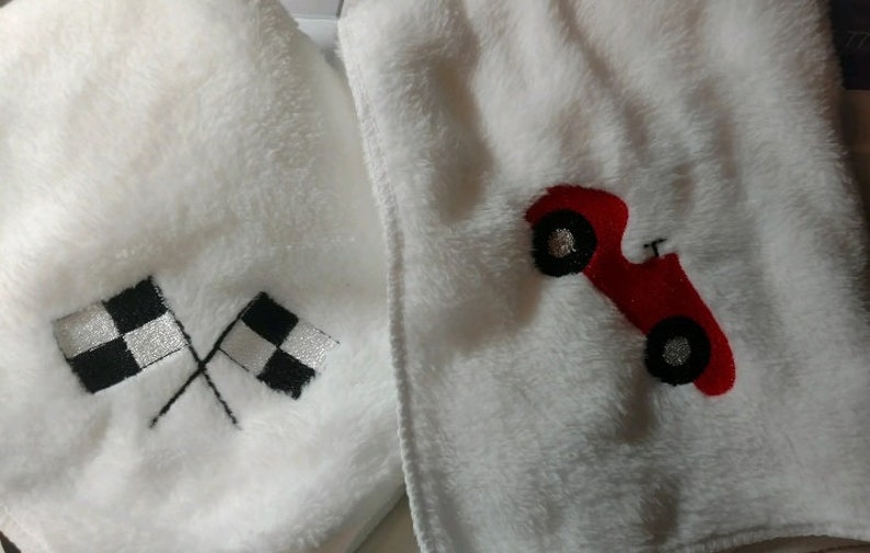 Pu&ograve; includere: Due coperte per bambini in peluche bianco con disegni ricamati. Una coperta presenta un'auto da corsa rossa con ruote nere. L'altra coperta presenta due bandiere a scacchi bianche e nere.