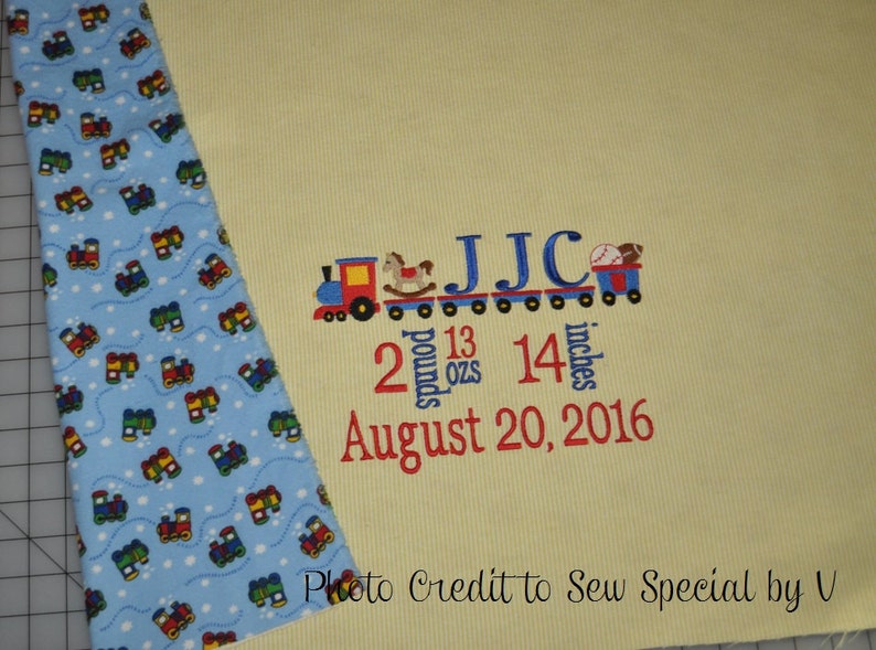 May include: A yellow baby blanket with a blue and white train pattern border. The blanket is embroidered with a train carrying the letters JJC, the numbers 2 pounds 13 ounces and 14 inches, and the date August 20, 2016.