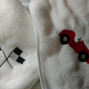 Pu&ograve; includere: Due coperte per bambini in peluche bianco con disegni ricamati. Una coperta presenta un'auto da corsa rossa con ruote nere. L'altra coperta presenta due bandiere a scacchi bianche e nere.