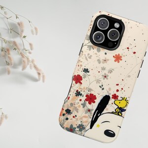 May include: A phone case featuring a floral pattern and a cartoon illustration of Snoopy and Woodstock. The case has a cream-coloured background with red, grey, and white flowers. Snoopy and Woodstock are on the bottom right.