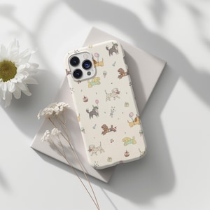 Puede incluir: Funda de teléfono crema con un patrón repetido de perros de dibujos animados, globos, conos de helado y pastelitos. La funda tiene un parachoques protector y un recorte para la cámara.