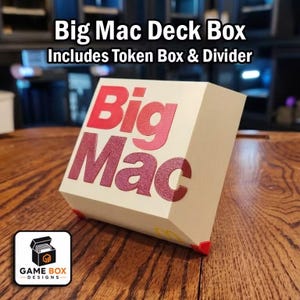 May include: A cream-colored deck box featuring the red text Big Mac on the front. The box includes a token box and divider. The design includes small red corner accents and a yellow logo on the bottom edge. The text Big Mac Deck Box Includes Token Box & Divider is displayed above the object.