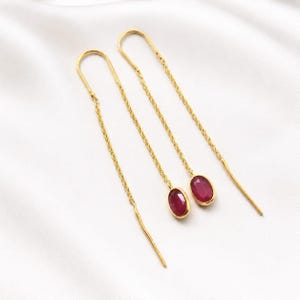 Puede incluir: Un par de pendientes de hilo de oro con cadenas largas y delicadas y piedras preciosas de rubí rojo intenso de forma ovalada engastadas en biseles de oro liso. Los pendientes están diseñados para pasarse a través del lóbulo de la oreja.