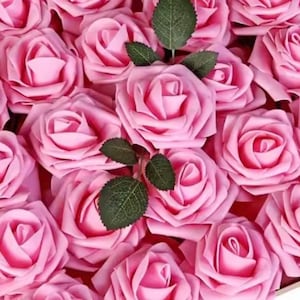 Puede incluir: Primer plano de una colección de rosas artificiales rosas. Las rosas están en plena floración, con múltiples pétalos y una textura suave y aterciopelada. Hojas verdes se intercalan entre las flores, agregando un toque de contraste. El efecto general es un arreglo floral romántico y delicado.