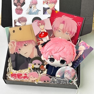 May include: A collection of anime-style merchandise featuring a character with pink hair, including a plush doll with a mushroom accessory, acrylic stands, a button pin, stickers, and printed cards, all arranged inside a black cardboard box.