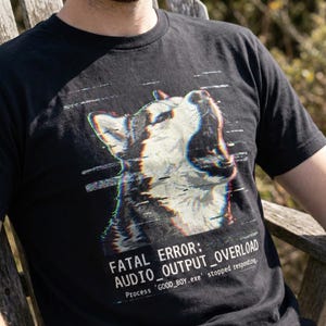 May include: Black t-shirt with a glitch-effect image of a dog. The text reads "FATAL ERROR: AUDIO_OUTPUT_OVERLOAD" and "Process 'GOOD_BOY.exe' stopped responding." The dog graphic is in white, grey, and black.