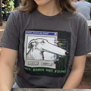 May include: Dark grey t-shirt with a graphic of a long-nosed dog in a computer error window. The text reads "SNOOT_OVERFLOW_ERROR" and "404: BRAIN NOT FOUND". The design includes the options "[PET]" and "[REBOOT]" at the bottom.