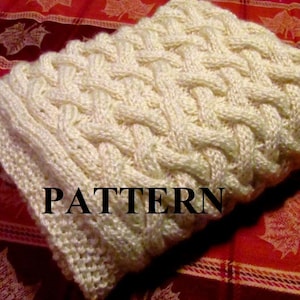 May include: A close-up of a white knitted scarf with a cable knit pattern. The scarf is lying on a red and white patterned fabric. The word "PATTERN" is printed in black letters on the scarf.