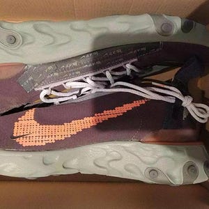 May include: Pair of Nike React Element 55 trainers in a box. The shoes have a dark purple upper with an orange Nike swoosh. The sole is light green with a unique design. White laces and a grey tongue complete the look.