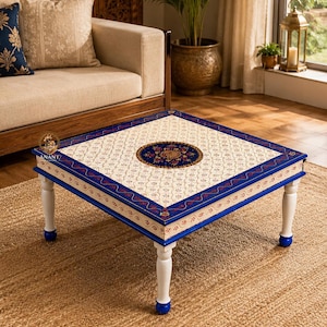 May include: A square coffee table featuring a cream-coloured top with a repeating floral pattern and a central dark blue circular medallion. The table has a blue border with red floral accents and four white turned legs with blue feet.