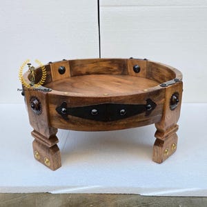 May include: A round, wooden side table with a dark brown finish. The table features a raised rim, decorative metal accents, and four sturdy legs. The table is approximately 12 inches in diameter and 8 inches tall.