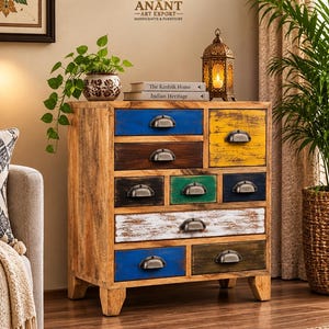 May include: A wooden chest of drawers featuring a natural light brown finish and nine drawers of varying sizes. Each drawer is painted in different colors including blue, yellow, dark brown, green, black, and white, and fitted with metal cup pulls.