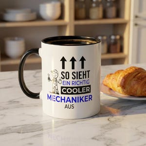 May include: White ceramic coffee mug with a black handle and rim. The mug features the text "SO SIEHT EIN RICHTIG COOLER MECHANIKER AUS" in black and blue, along with a cartoon mechanic illustration.