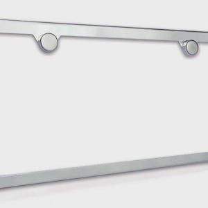 May include: A shiny, silver-colored license plate frame with rounded corners. The frame has two small, circular mounting posts. The frame is designed to hold a standard-sized license plate.