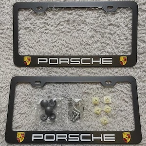 May include: Two black license plate frames with the word "PORSCHE" in white lettering. Each frame has the Porsche emblem on both ends. Hardware, including screws and mounting clips, is included.