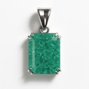 Puede incluir: Colgante rectangular de piedra verde con fianza y cuatro garras plateadas. La piedra preciosa tiene un aspecto texturizado y está engastada en un engaste de metal plateado. El colgante se muestra sobre un fondo blanco.