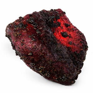 May include: A close-up of a dark red object with a textured surface and black spots. The object has a bright red area on one side. The background is white.