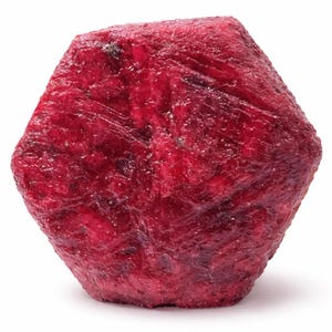 Puede incluir: Una gema de rubí en bruto sin cortar. El rubí es de un color rojo intenso y saturado con una superficie ligeramente texturizada. La gema tiene forma hexagonal y parece sin pulir, mostrando su forma natural. Ideal para anuncios de joyería y gemas.