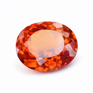 Könnte beinhalten: Ein oval geschliffener, facettierter Edelstein in Orange- und Rottönen. Der Edelstein hat eine polierte, reflektierende Oberfläche und ist vor einem weißen Hintergrund platziert. Die Facetten des Edelsteins fangen das Licht ein und erzeugen einen funkelnden Effekt. Geeignet für Schmuck.