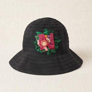 May include: A black bucket hat featuring a horizontal ribbed texture and a prominent central floral applique. The applique is crafted from red beads, green embroidered leaves, and small pink and yellow accents, creating a detailed design.