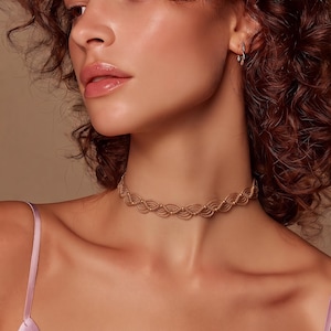 May include: A beige macrame choker necklace featuring a repeating wave pattern constructed from thin cord, accented with small, evenly spaced metallic gold beads integrated into the centre of each curved loop along the entire length of the band.