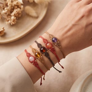 May include: Five macrame bracelets featuring central round gemstones in shades of purple, orange, dark red, yellow, and light pink. Each bracelet is crafted with knotted cord in matching or complementary colours, accented with small metallic beads.