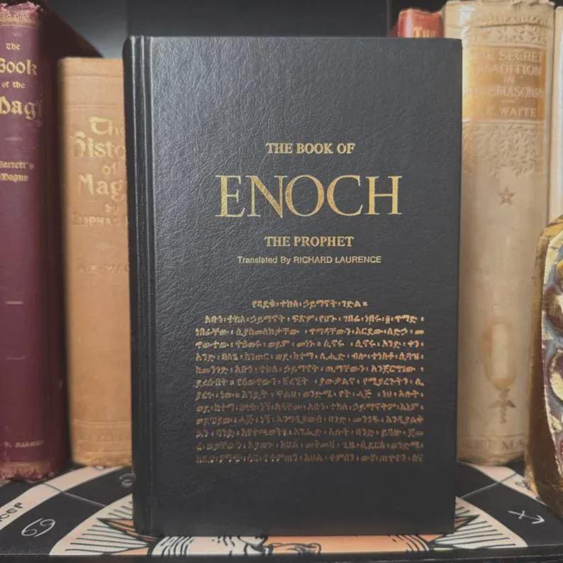 May include: A hardcover book titled "The Book of Enoch" with gold lettering on a black cover. The book's title and author are displayed prominently. Additional text in a smaller font is also visible. The book is part of a collection.