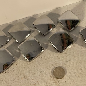 May include: Eight silver square cabinet knobs with a reflective surface. The knobs are arranged in a semi-circle on a white surface.