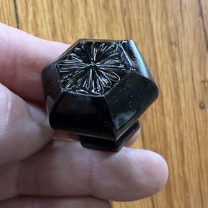May include: A black glass cabinet knob with a geometric shape and a floral design.