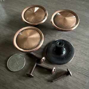 May include: Four antique copper cabinet knobs with a black knob and screws. The knobs have a raised, circular design.