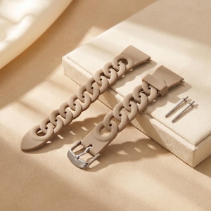 May include: Two tan watch bands with a chain link design. One band has a silver buckle, and the other has a clasp. Two silver pins are also included. The bands are made of a soft, flexible material.