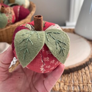 Close-up of a red patchwork apple showing hand stitched green felt leaves and cinnamon stick stem.