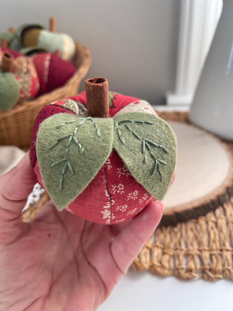 Close-up of a red patchwork apple showing hand stitched green felt leaves and cinnamon stick stem.