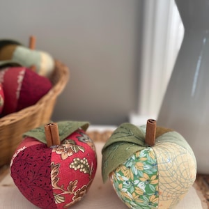 Two handmade patchwork apples in red and green fabrics with cinnamon stems and felt leaves.