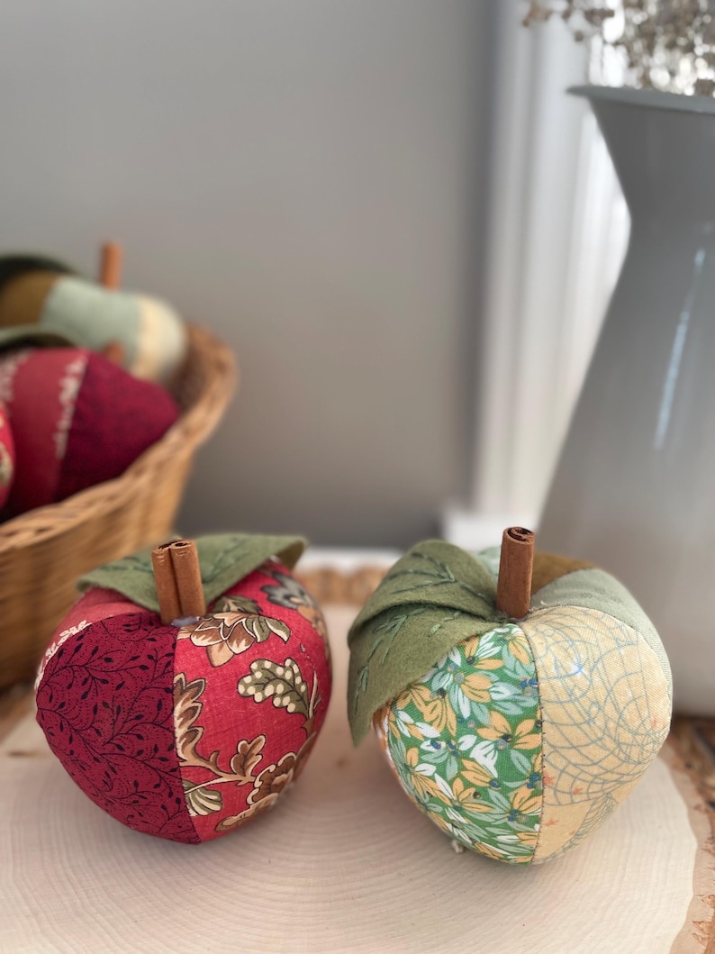 Two handmade patchwork apples in red and green fabrics with cinnamon stems and felt leaves.