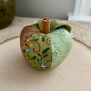 Close-up of a green patchwork fabric apple showing its handmade construction, felt leaves and cinnamon stem.