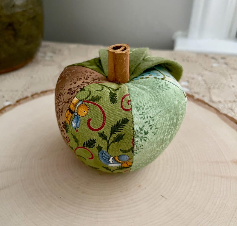 Close-up of a green patchwork fabric apple showing its handmade construction, felt leaves and cinnamon stem.